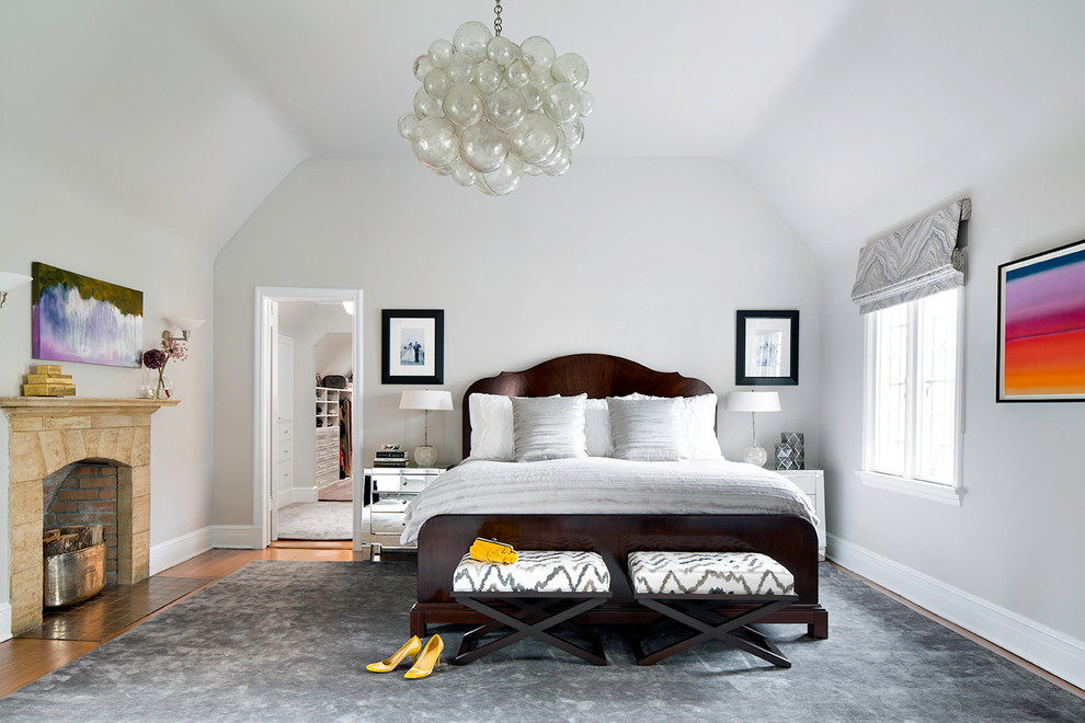 Ispirazione per una camera da letto classica con pareti grigie, pavimento in legno massello medio, camino classico e cornice del camino in pietra