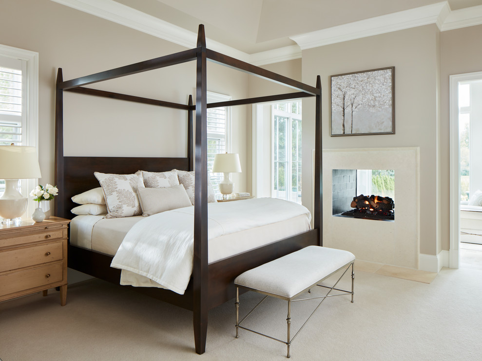 На фото: спальня в стиле неоклассика (современная классика) с бежевыми стенами, ковровым покрытием, двусторонним камином и бежевым полом