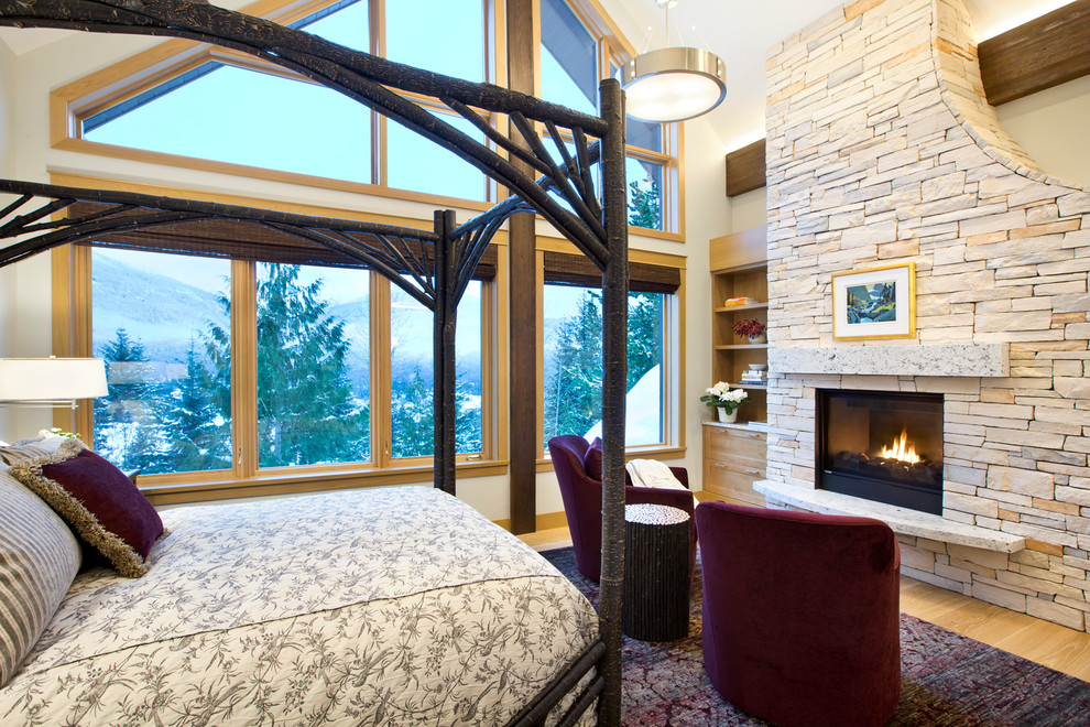 Example of a large mountain style master light wood floor and beige floor bedroom design in Other with a standard fireplace, a stone fireplace and gray walls
