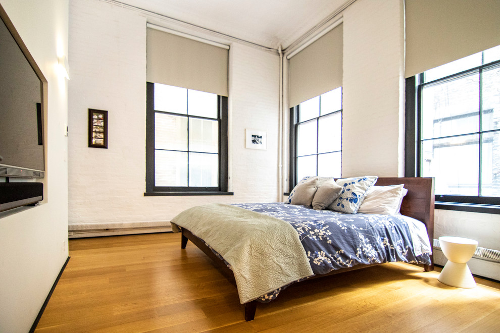Großes Industrial Hauptschlafzimmer mit weißer Wandfarbe, hellem Holzboden und braunem Boden in New York