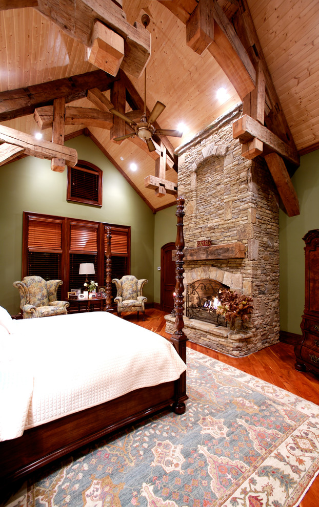 Expansive rustic master bedroom in Other with green walls, medium hardwood flooring, a standard fireplace and a stone fireplace surround.