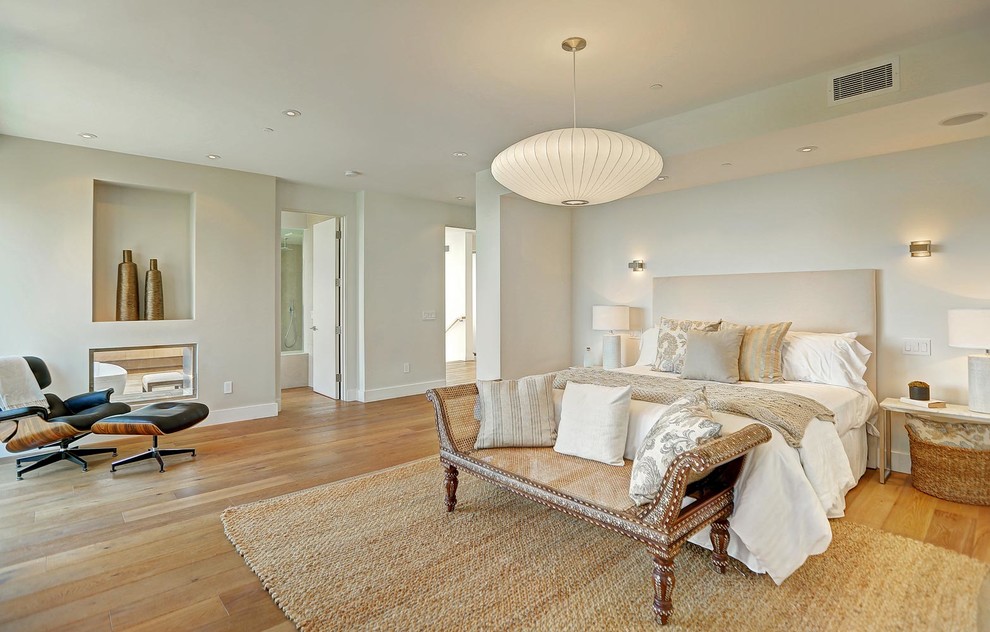 Aménagement d'une grande chambre parentale moderne avec un mur beige, un sol en bois brun, une cheminée double-face et un manteau de cheminée en métal.