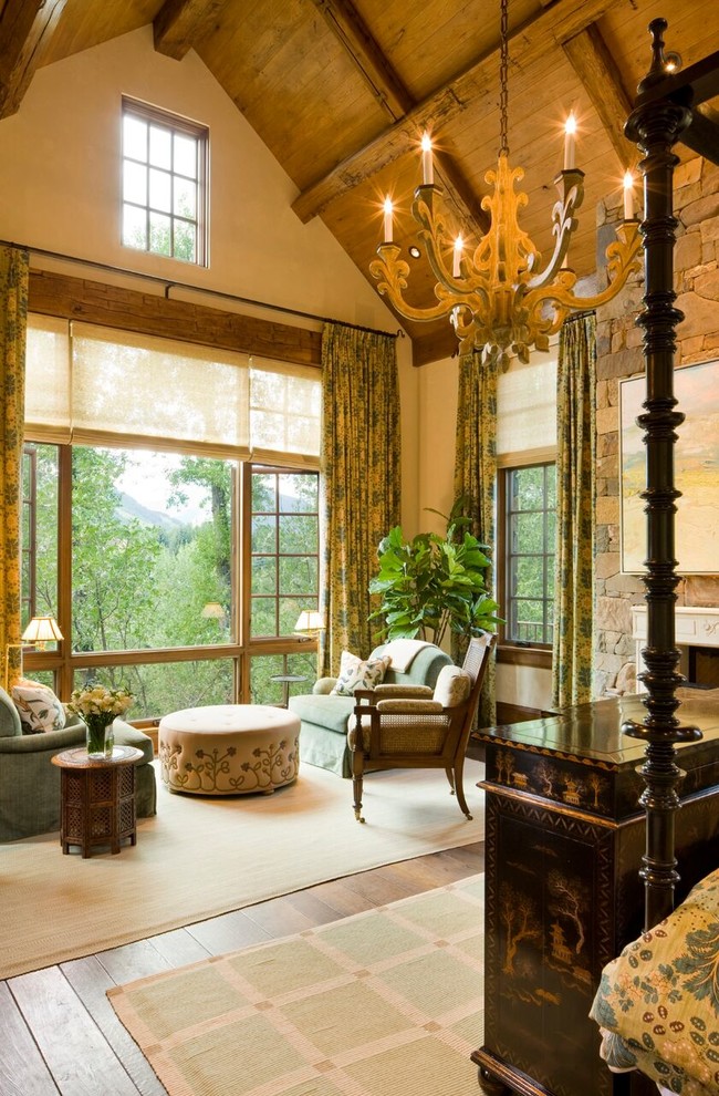 Ejemplo de dormitorio principal de estilo americano grande con paredes blancas, suelo de madera en tonos medios, todas las chimeneas, marco de chimenea de piedra y suelo marrón