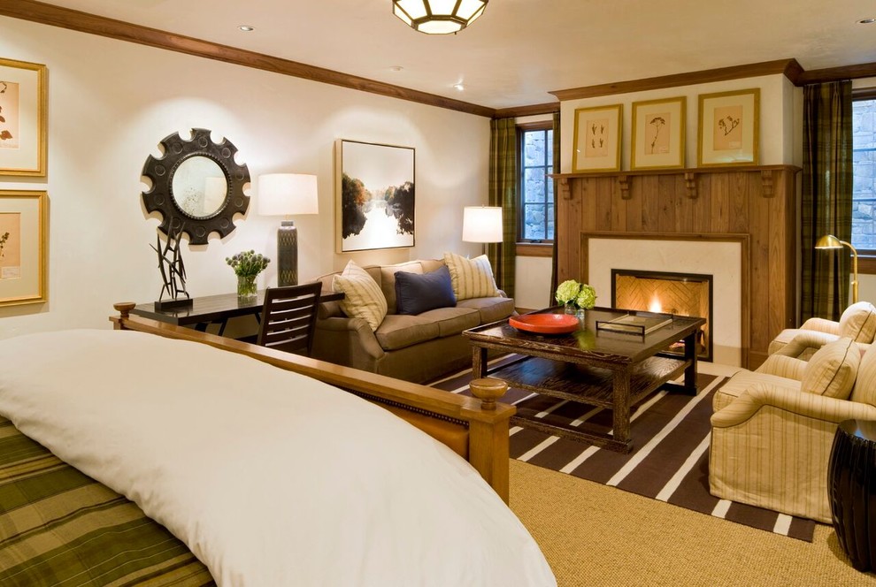 Modelo de dormitorio principal de estilo americano grande con paredes blancas, moqueta, todas las chimeneas, marco de chimenea de piedra y suelo blanco