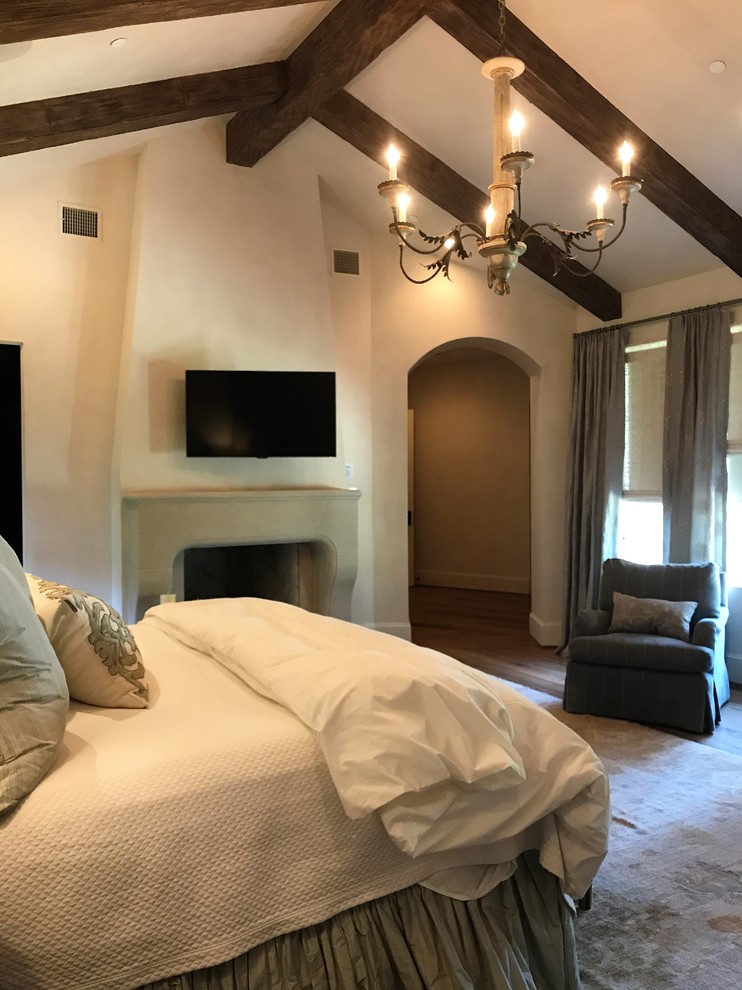 Modelo de dormitorio principal mediterráneo con paredes beige, suelo de madera oscura, todas las chimeneas y marco de chimenea de yeso