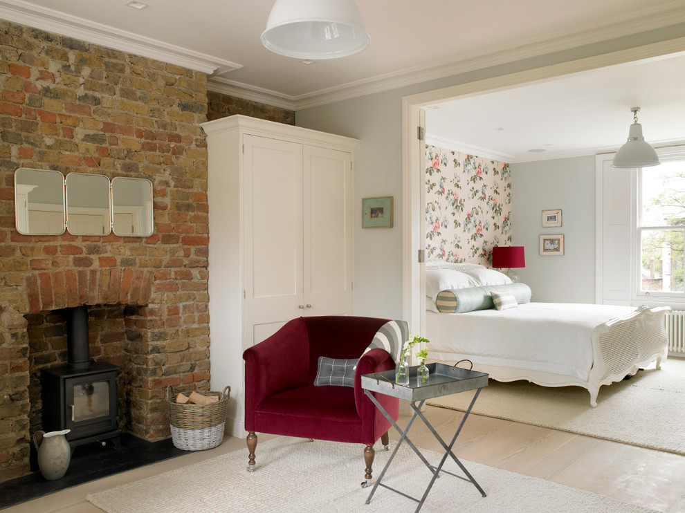 Klassisches Schlafzimmer mit grauer Wandfarbe, hellem Holzboden, Kaminumrandung aus Backstein und Kaminofen in London