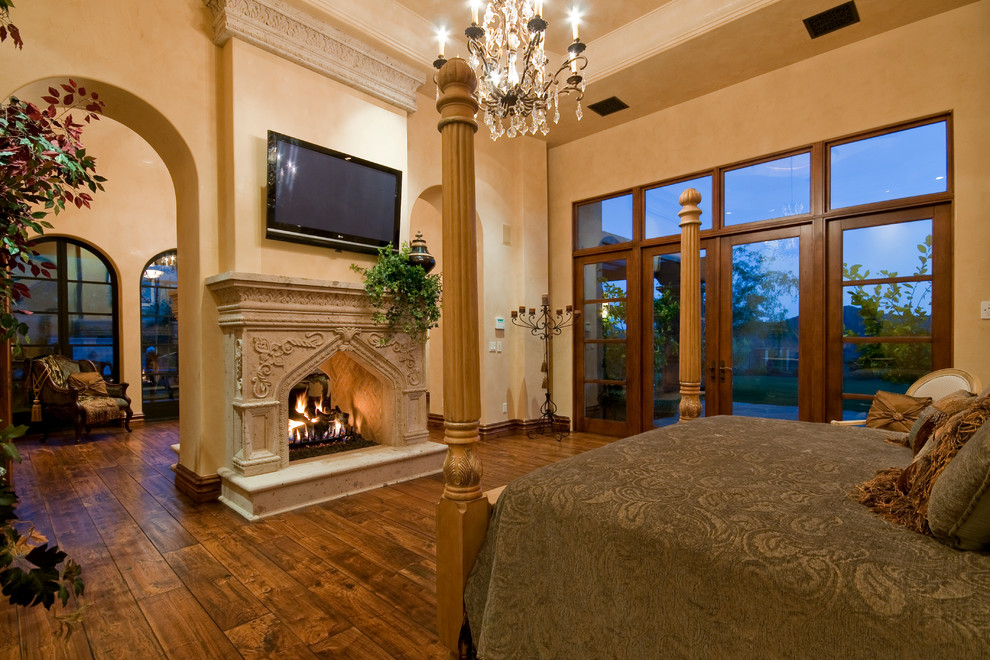 Foto de dormitorio principal tradicional extra grande con paredes beige, suelo de madera en tonos medios, chimenea de doble cara y marco de chimenea de piedra