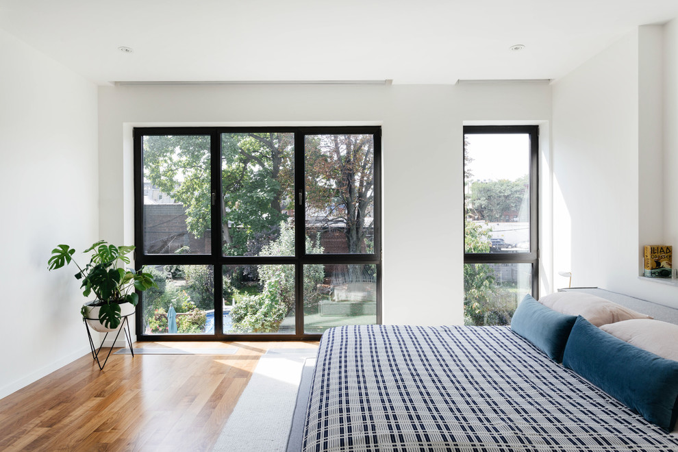 Mittelgroßes Modernes Hauptschlafzimmer mit weißer Wandfarbe, dunklem Holzboden, Kamin, Kaminumrandung aus Stein und braunem Boden in New York