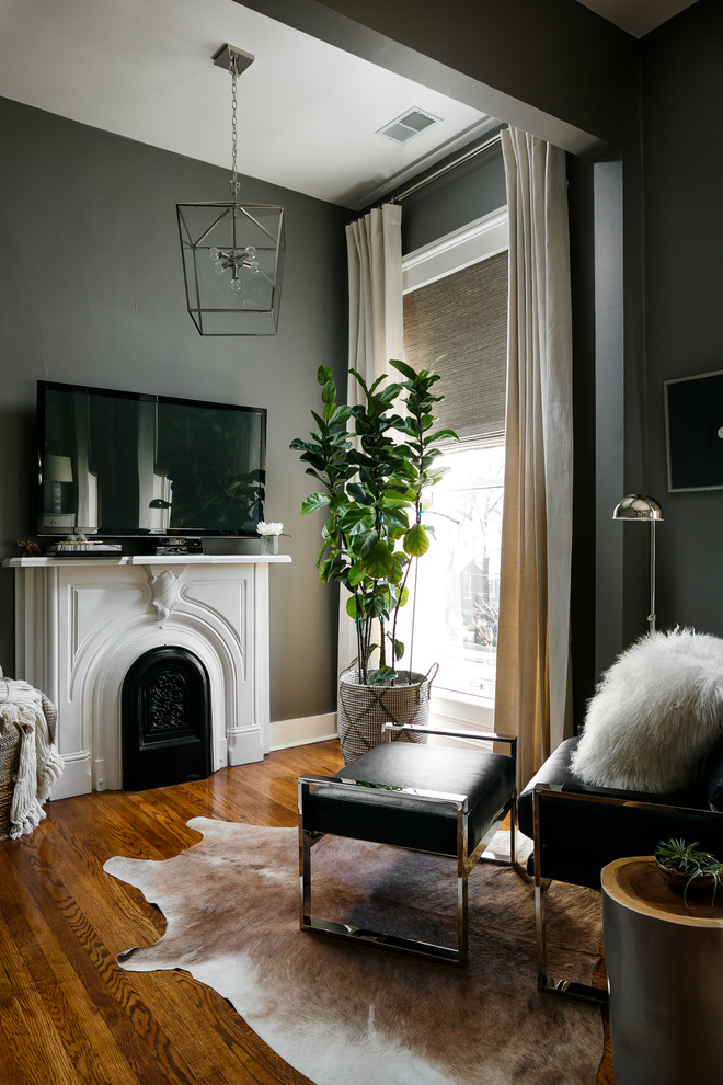 Cette photo montre une chambre parentale moderne de taille moyenne avec un mur gris, un sol en bois brun, une cheminée standard, un manteau de cheminée en bois et un sol marron.