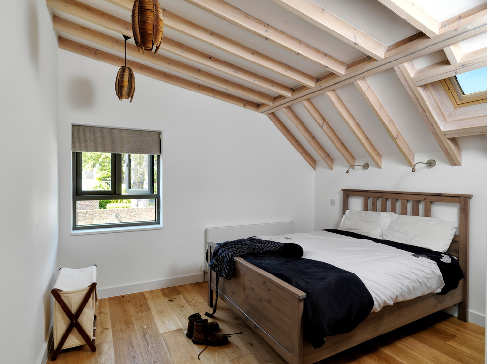 Photo of a large contemporary guest loft bedroom in London with white walls and light hardwood flooring.