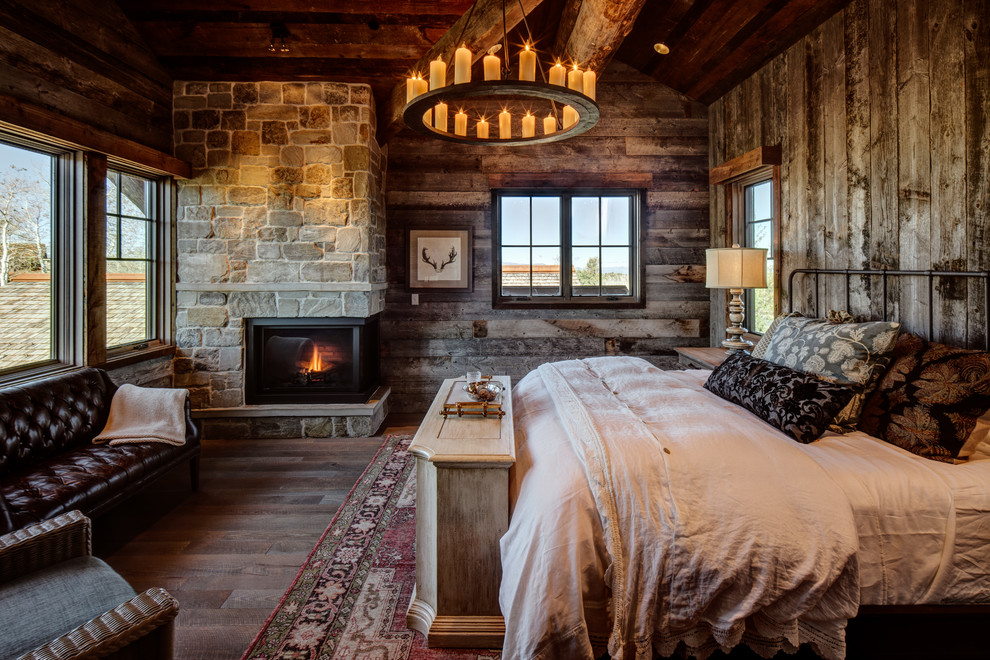Cette image montre une chambre d'amis chalet avec une cheminée d'angle, un manteau de cheminée en pierre, un sol marron, un mur marron et parquet foncé.