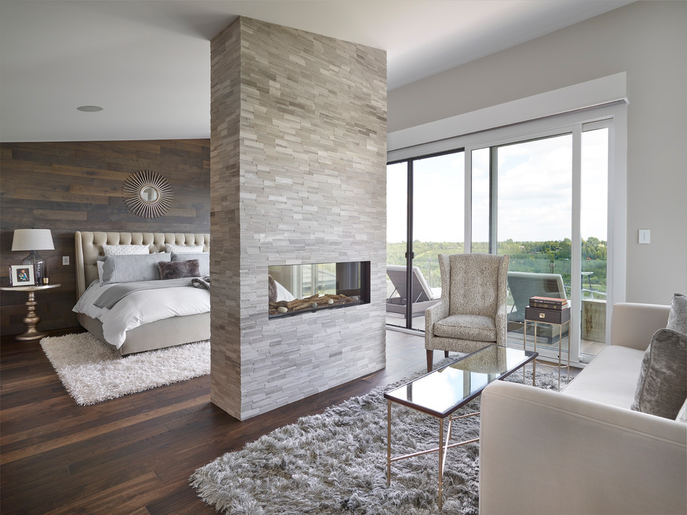 Стильный дизайн: спальня в стиле неоклассика (современная классика) с серыми стенами, темным паркетным полом, двусторонним камином, фасадом камина из камня и коричневым полом - последний тренд