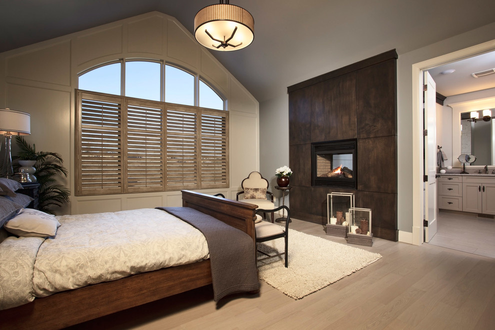 Modelo de dormitorio principal clásico grande con paredes grises, suelo de madera oscura, chimenea de doble cara y marco de chimenea de baldosas y/o azulejos