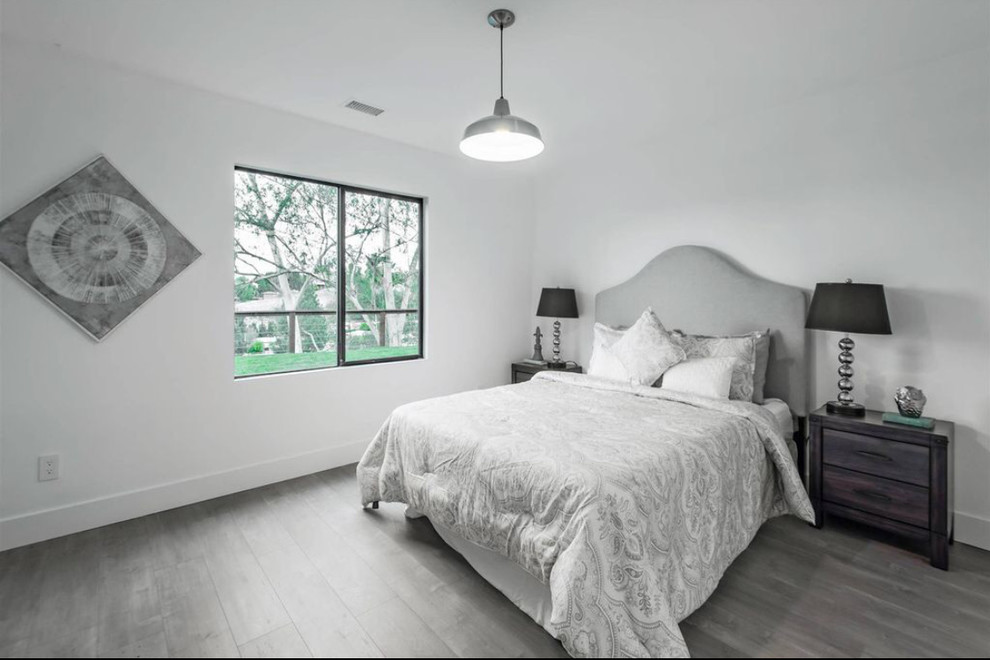 Modelo de habitación de invitados moderna grande sin chimenea con paredes blancas, suelo laminado y suelo gris