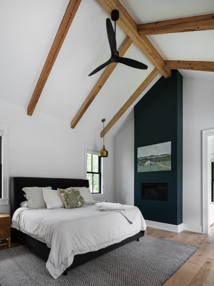 Cette image montre une chambre parentale rustique de taille moyenne avec un mur blanc, un sol en bois brun, une cheminée standard, un manteau de cheminée en plâtre, un sol marron et un plafond voûté.