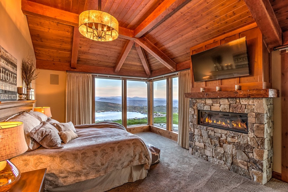 На фото: большая хозяйская спальня в стиле рустика с коричневыми стенами, ковровым покрытием, горизонтальным камином, фасадом камина из камня и серым полом с