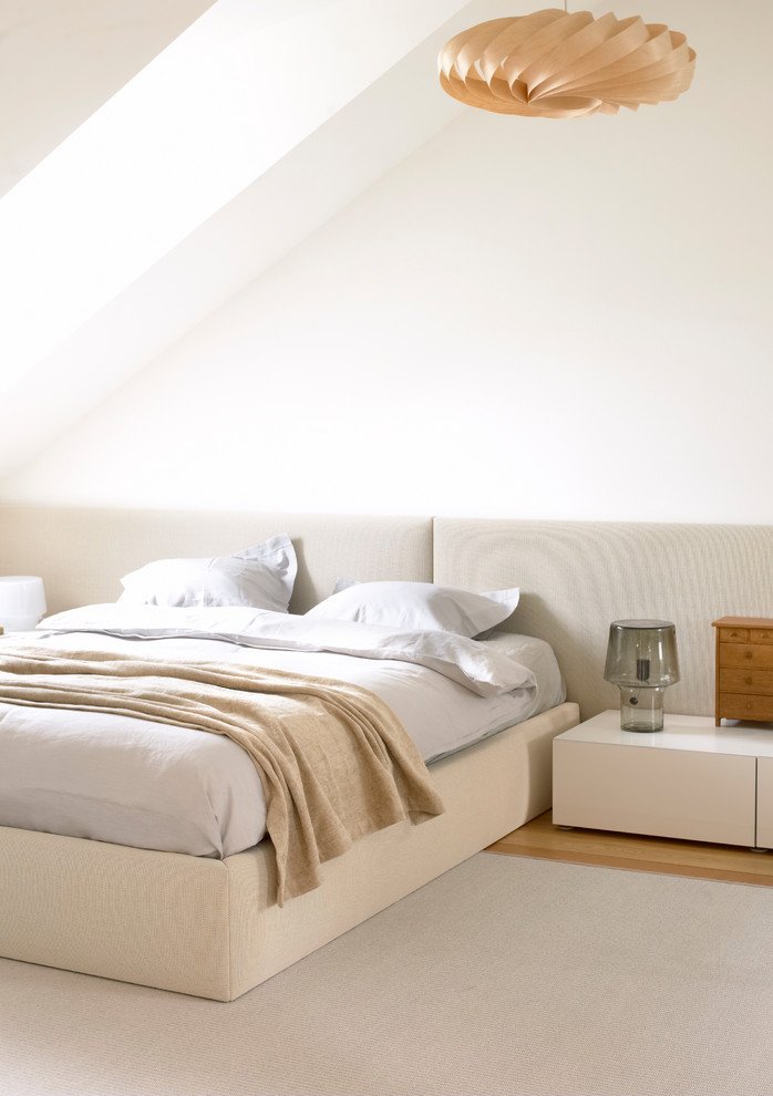 Modelo de dormitorio principal minimalista grande sin chimenea con paredes blancas y suelo de madera clara