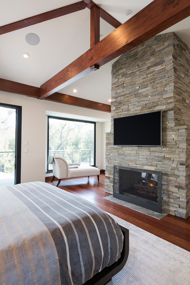 Geräumiges Modernes Hauptschlafzimmer mit weißer Wandfarbe, braunem Holzboden, Tunnelkamin, Kaminumrandung aus Stein und braunem Boden in San Diego
