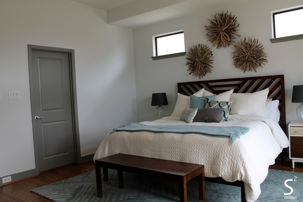 Cette image montre une grande chambre parentale vintage avec un mur blanc et un sol en bois brun.