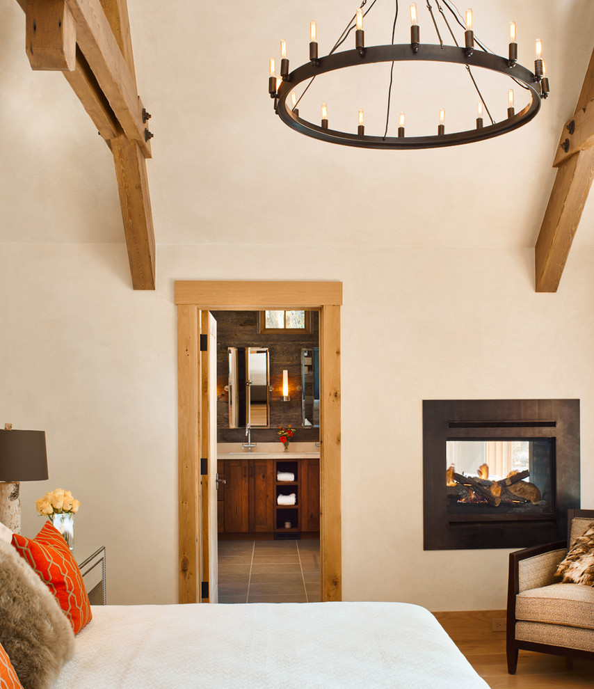 Aménagement d'une chambre montagne avec un mur beige, un sol en bois brun et une cheminée double-face.