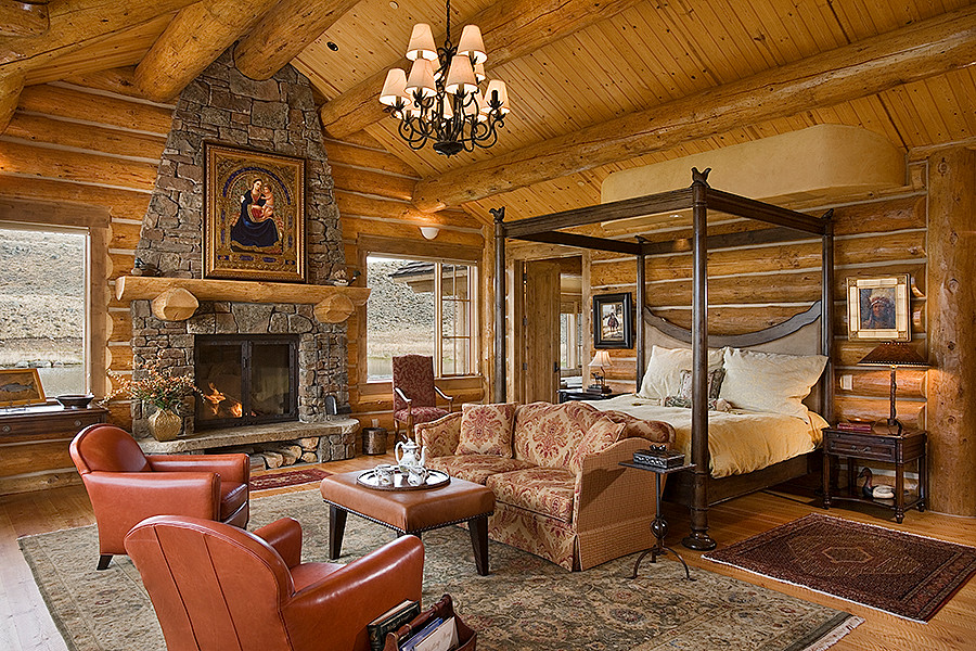 Foto de dormitorio principal rural grande con suelo de madera en tonos medios, todas las chimeneas y marco de chimenea de piedra