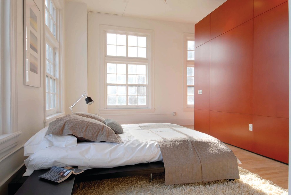 Esempio di una camera da letto minimalista con pareti arancioni e parquet chiaro