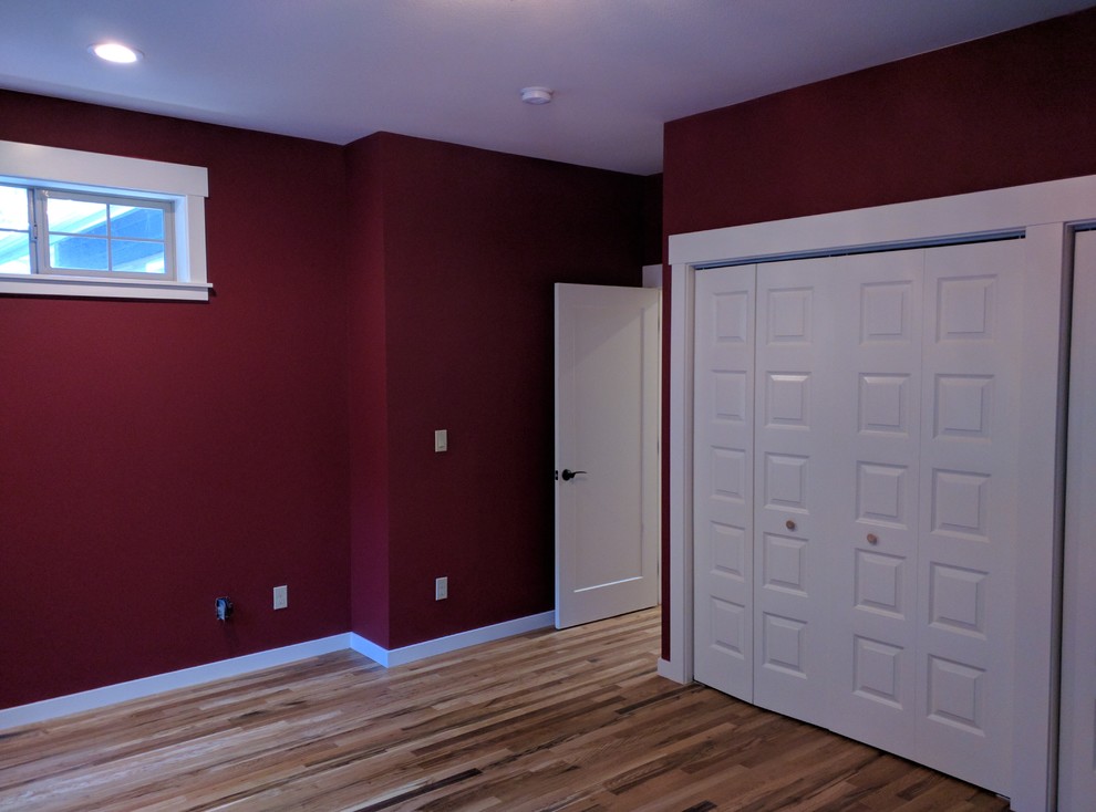 Imagen de dormitorio principal de estilo americano de tamaño medio sin chimenea con paredes rojas y suelo de madera en tonos medios