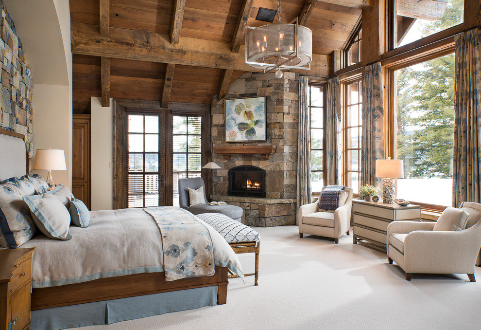 Стильный дизайн: хозяйская спальня в стиле рустика с ковровым покрытием, угловым камином, фасадом камина из камня и бежевым полом - последний тренд