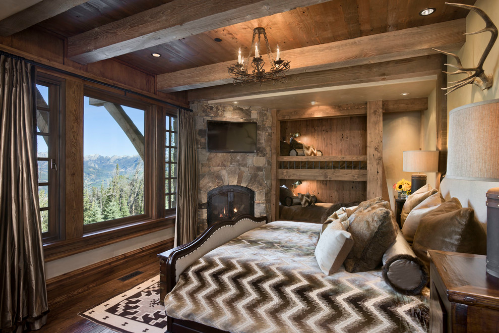 Ejemplo de habitación de invitados rústica con paredes beige, suelo de madera oscura, chimenea de esquina y marco de chimenea de piedra