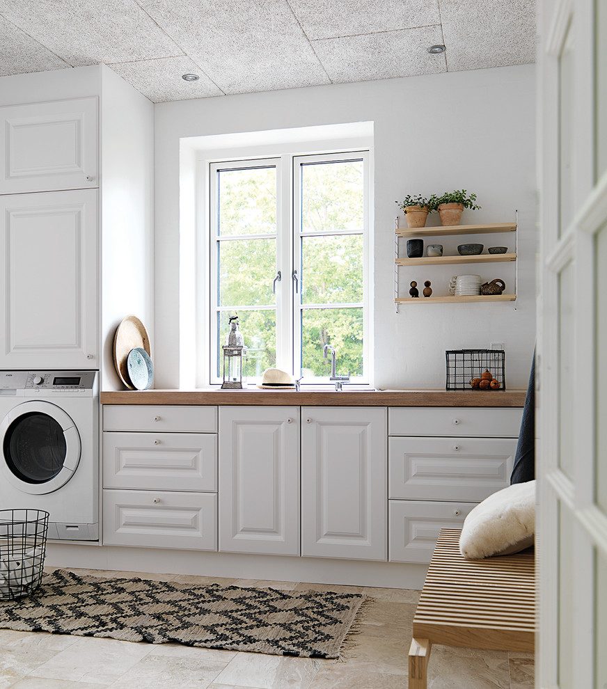 Design ideas for a medium sized farmhouse single-wall utility room with a built-in sink, raised-panel cabinets, white cabinets, wood worktops, white walls and ceramic flooring.