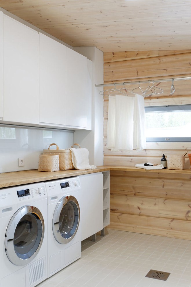 Immagine di una lavanderia multiuso nordica di medie dimensioni con ante lisce, ante bianche, top in legno, pareti beige, pavimento con piastrelle in ceramica, lavatrice e asciugatrice affiancate e top beige