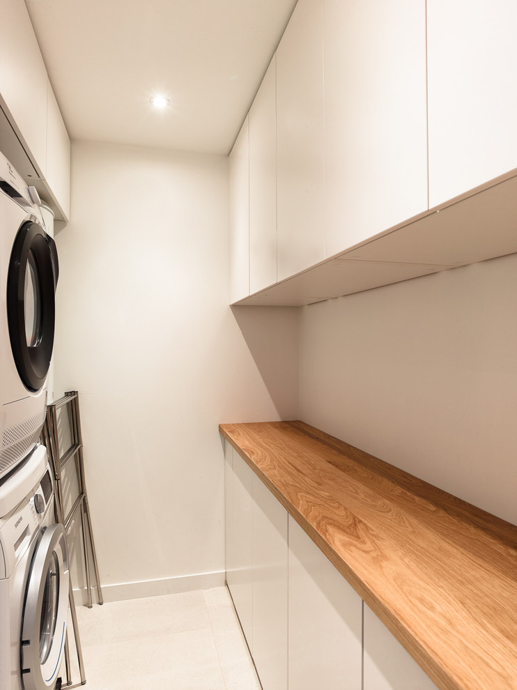 This is an example of a medium sized contemporary single-wall separated utility room in Paris with white cabinets, wood worktops, white walls, ceramic flooring, a stacked washer and dryer, beige floors and brown worktops.