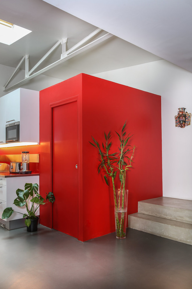 Foto de cuarto de lavado de galera urbano pequeño con armarios con paneles empotrados, puertas de armario rojas, encimera de vidrio y encimeras rojas
