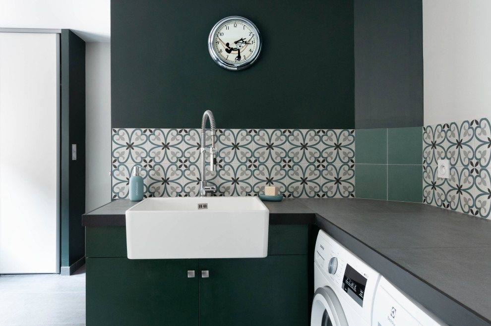 リヨンにある広いインダストリアルスタイルのおしゃれな家事室 (シングルシンク、タイルカウンター、緑の壁、セラミックタイルの床、左右配置の洗濯機・乾燥機、グレーの床、グレーのキッチンカウンター) の写真