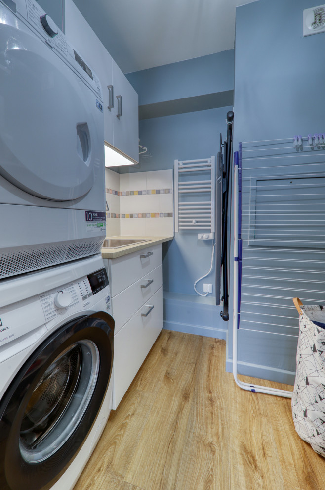 Immagine di una lavanderia multiuso bohémian con lavello sottopiano, ante bianche, top in laminato, pareti blu, pavimento in vinile e lavatrice e asciugatrice a colonna
