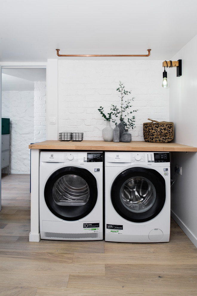 Immagine di una grande sala lavanderia nordica con top in legno, pareti bianche, parquet chiaro e lavatrice e asciugatrice affiancate