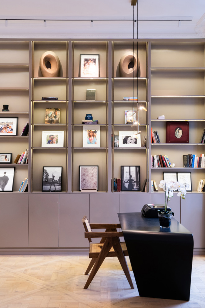 Cette photo montre un grand bureau tendance avec une bibliothèque ou un coin lecture, un mur beige, parquet clair, aucune cheminée, un bureau indépendant et un sol beige.