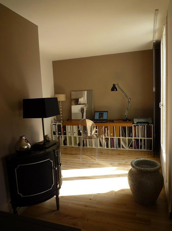 Modern inredning av ett mellanstort hemmabibliotek, med beige väggar, ljust trägolv, ett fristående skrivbord och beiget golv
