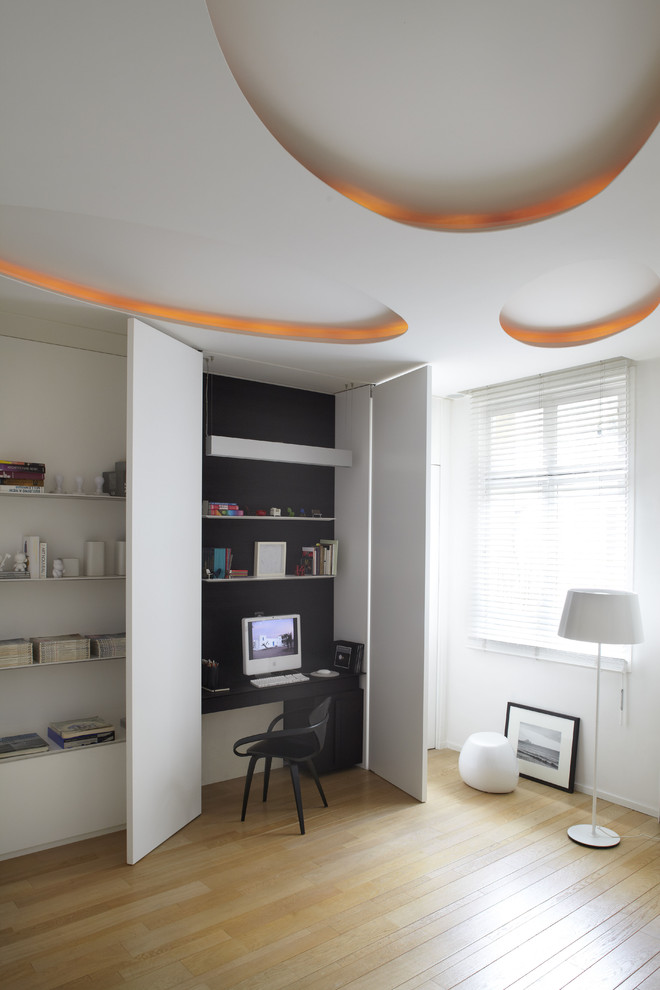 Inspiration för ett stort minimalistiskt hemmabibliotek, med vita väggar, ljust trägolv och ett inbyggt skrivbord