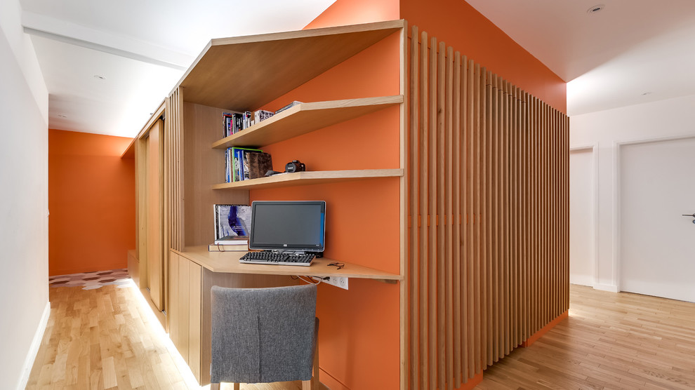 Kleines Modernes Arbeitszimmer ohne Kamin mit Arbeitsplatz, oranger Wandfarbe, hellem Holzboden und Einbau-Schreibtisch in Paris