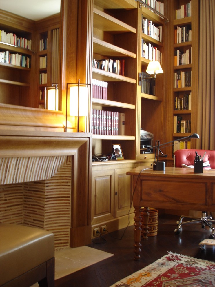 Modelo de despacho clásico renovado de tamaño medio con biblioteca, suelo de madera en tonos medios, todas las chimeneas, marco de chimenea de madera, escritorio independiente y suelo marrón