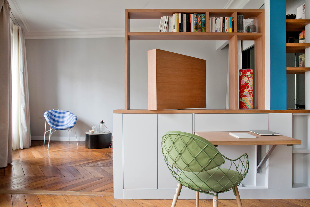 Small contemporary study in Paris with grey walls, medium hardwood flooring, a built-in desk and brown floors.