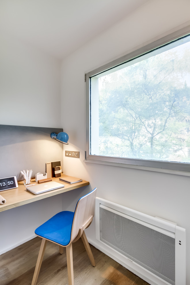 Kleines Skandinavisches Arbeitszimmer ohne Kamin mit Arbeitsplatz, weißer Wandfarbe, braunem Holzboden, Einbau-Schreibtisch und braunem Boden in Paris