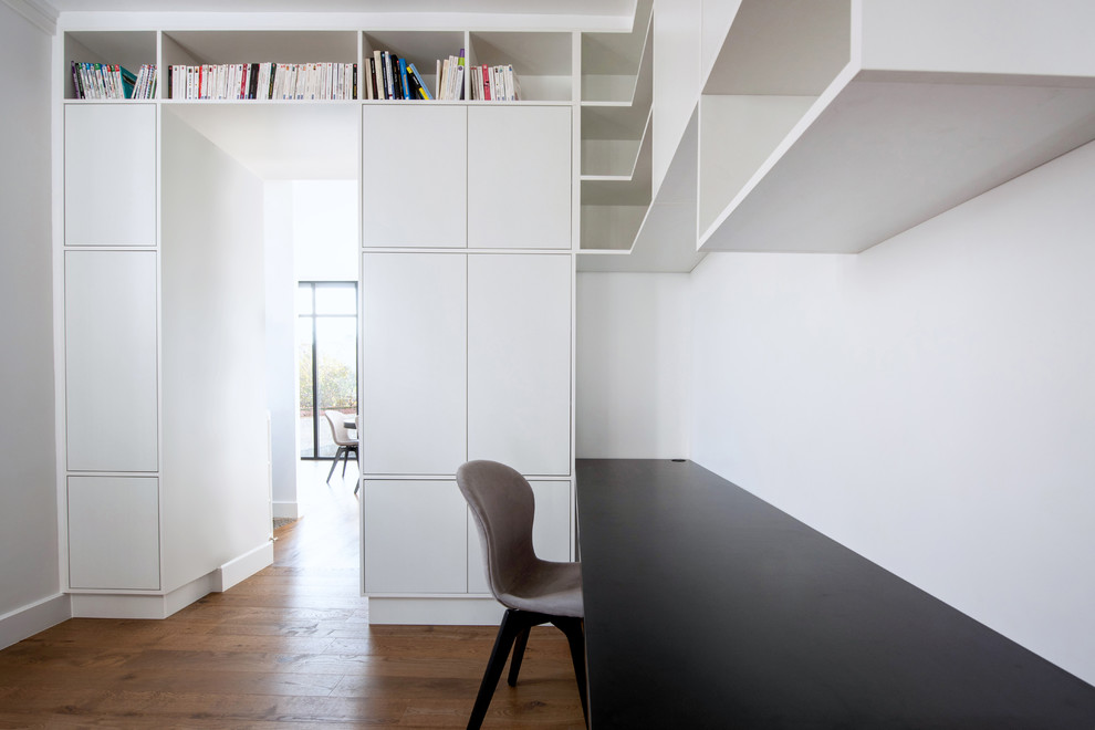 Cette image montre un bureau design de taille moyenne avec un mur blanc, parquet foncé, aucune cheminée, un bureau intégré et un sol marron.