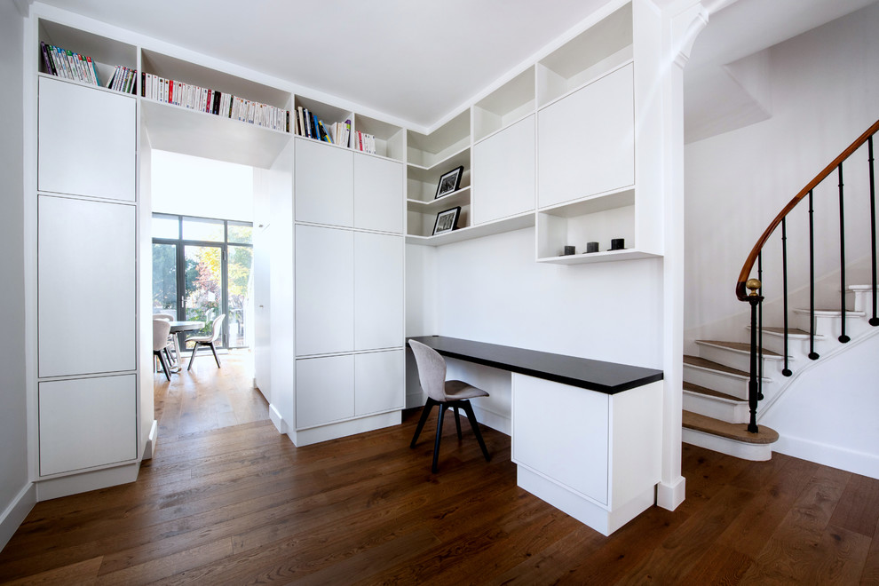 Medium sized contemporary study in Paris with white walls, dark hardwood flooring, no fireplace, a built-in desk and brown floors.