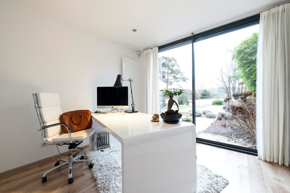 Diseño de despacho actual de tamaño medio sin chimenea con paredes blancas, suelo de madera clara y escritorio independiente