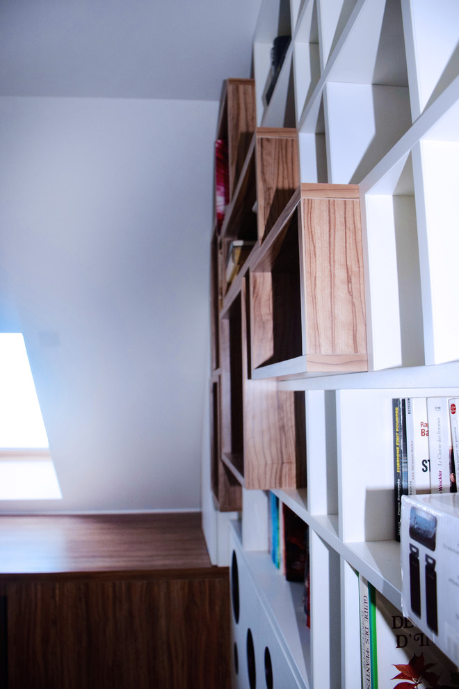 На фото: домашняя библиотека среднего размера в современном стиле с белыми стенами, светлым паркетным полом, встроенным рабочим столом и коричневым полом без камина