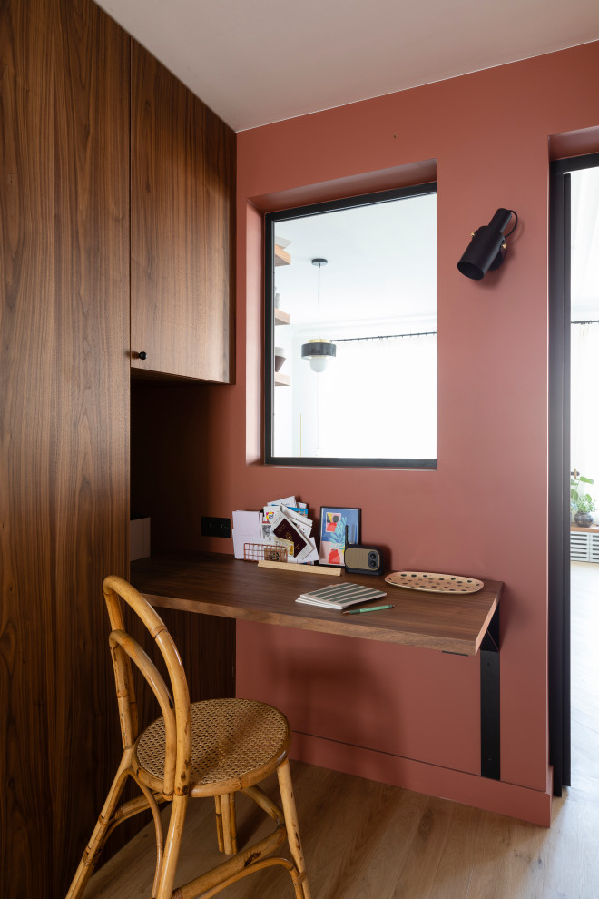 Mittelgroßes Modernes Arbeitszimmer mit Arbeitsplatz, roter Wandfarbe, hellem Holzboden und Einbau-Schreibtisch in Paris