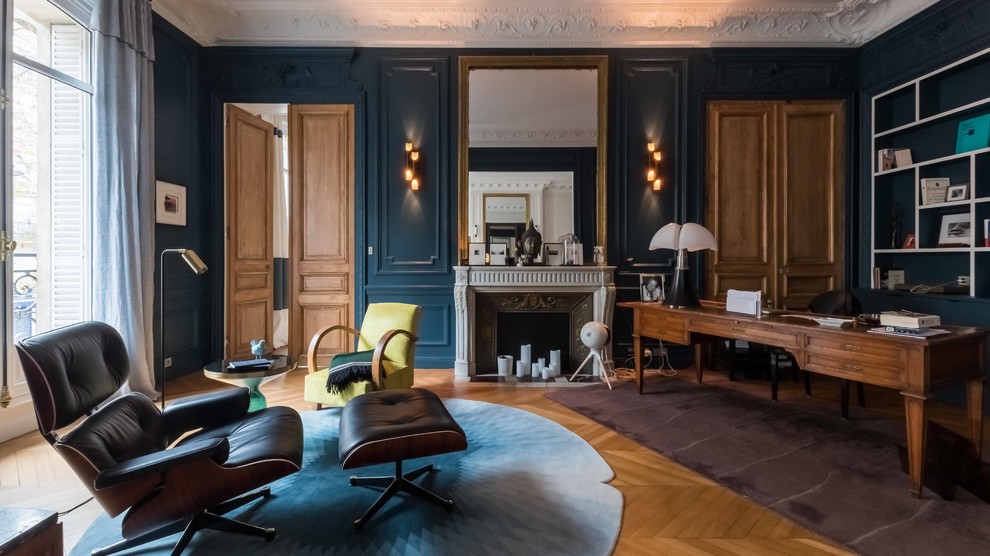 Classic study in Paris with blue walls, light hardwood flooring, a standard fireplace, a freestanding desk and brown floors.