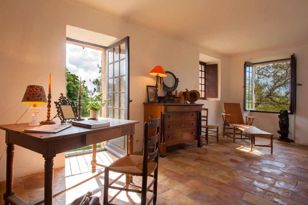 Mittelgroßes Landhausstil Arbeitszimmer mit beiger Wandfarbe, Terrakottaboden, freistehendem Schreibtisch und Arbeitsplatz in Korsika